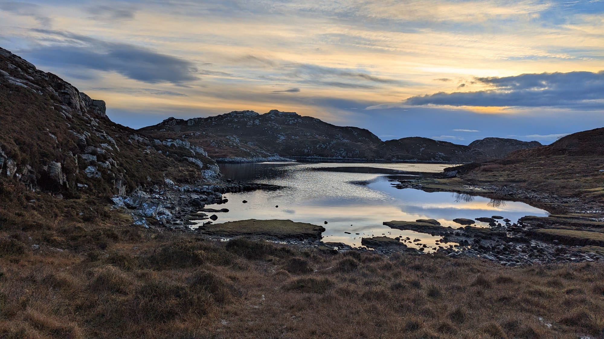 A rocky moorland landscape with loch in centre of photo and sunrise sky
