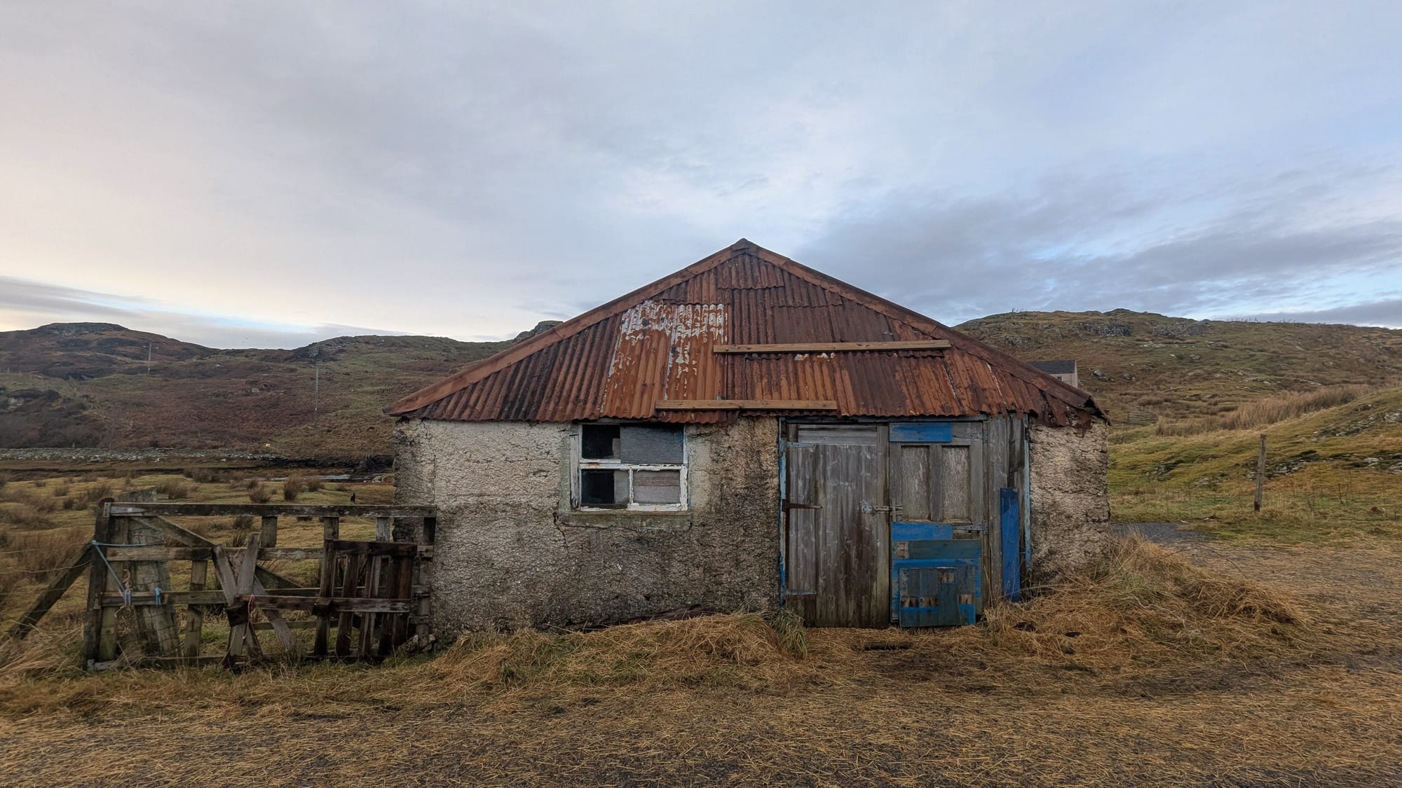 A stone built shed with rusty red tin roof and broken windows, in need of repair